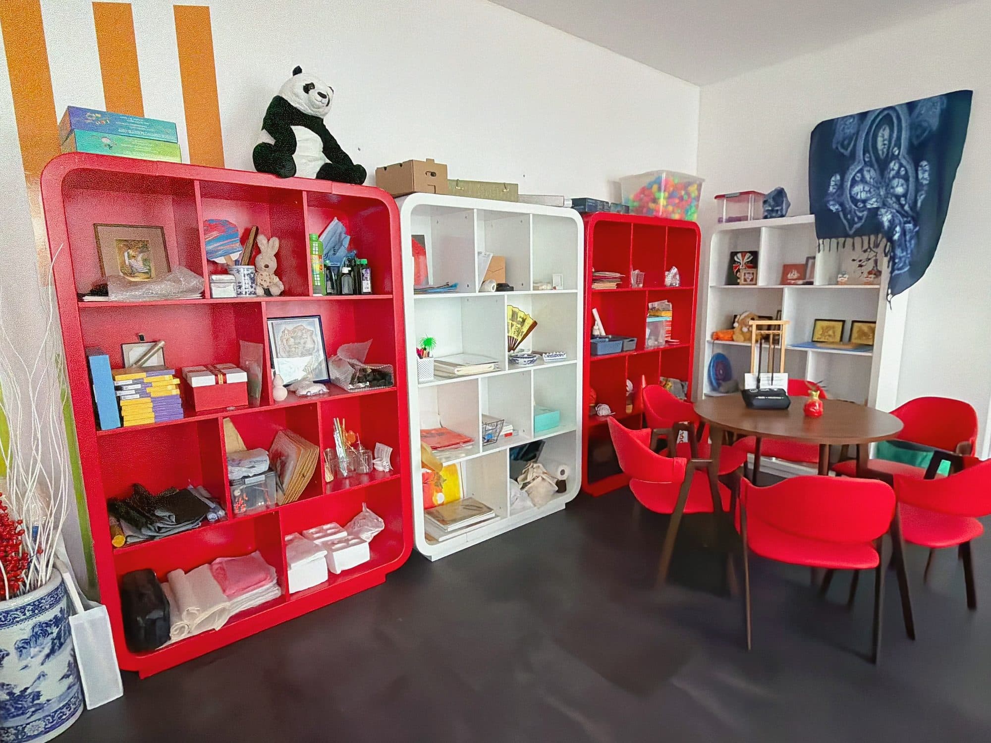 Begegnungsraum mit roten Regalen voller Bücher, Spielen und chinesischen Mitbringseln