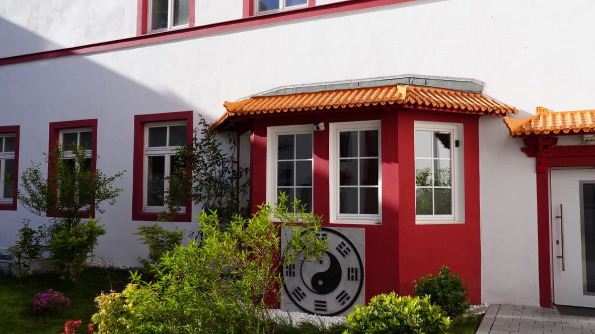 Rundes Yin-Yang-Medaillon an der Hauswand über einem bepflanzten Beet